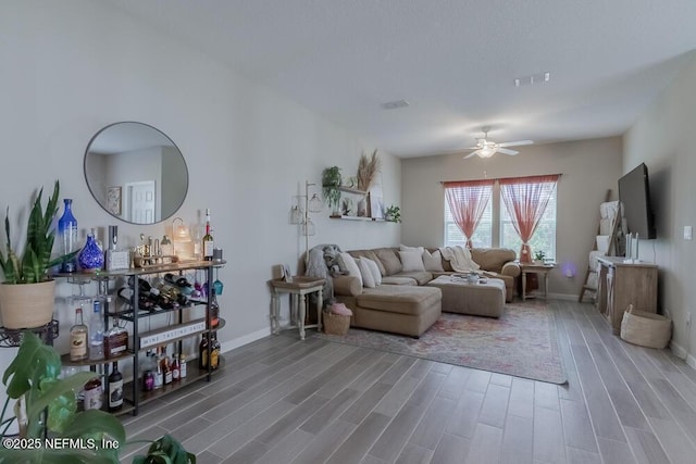 living room featuring visible vents, wood finished floors, baseboards, and ceiling fan