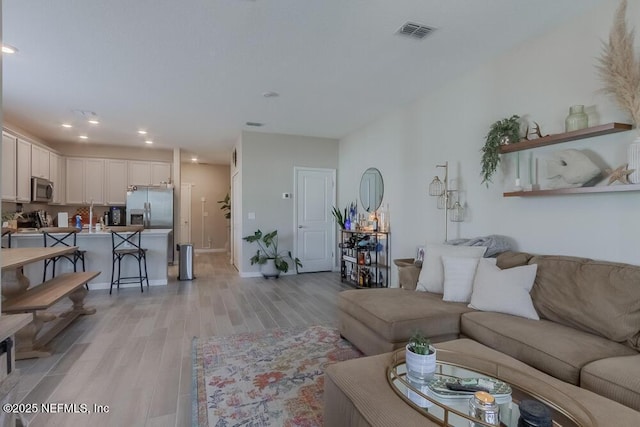 living area featuring light wood-style flooring, recessed lighting, visible vents, and baseboards