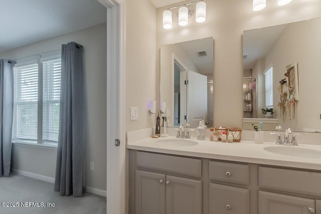 bathroom with double vanity, baseboards, visible vents, and a sink