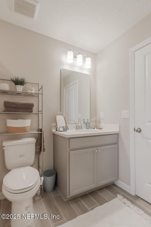 bathroom featuring visible vents, toilet, vanity, and wood finish floors