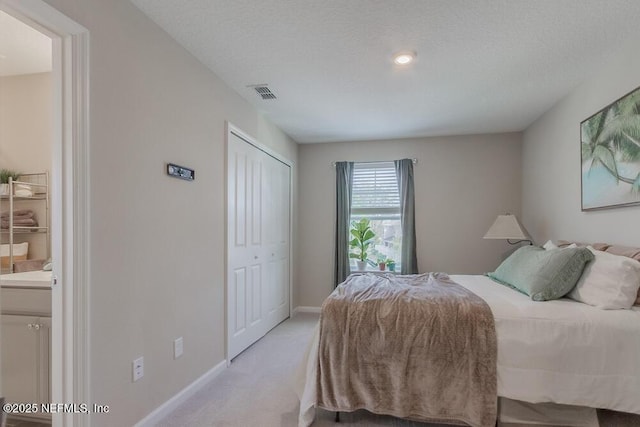 bedroom featuring visible vents, baseboards, light colored carpet, a closet, and ensuite bath