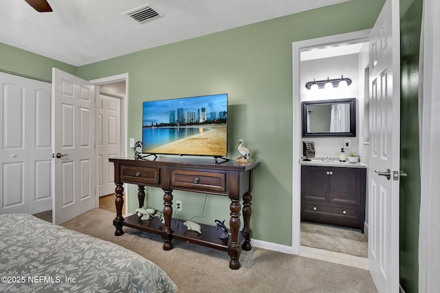 carpeted bedroom with visible vents, ensuite bathroom, baseboards, and a sink