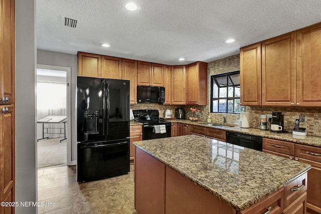 kitchen with visible vents, black appliances, a sink, light stone counters, and a kitchen island