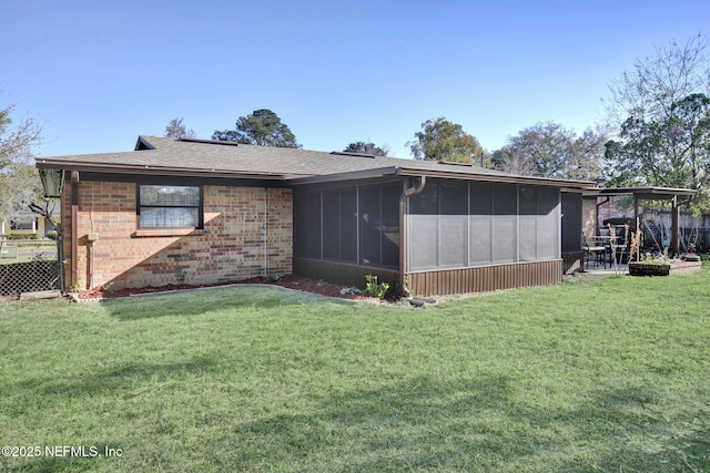 rear view of house featuring a yard, fence, brick siding, and a sunroom