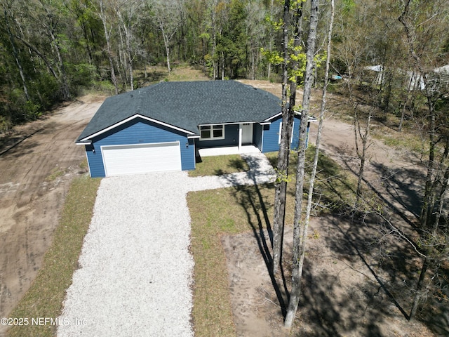 view of front of home featuring gravel driveway, a wooded view, a garage, and a shingled roof