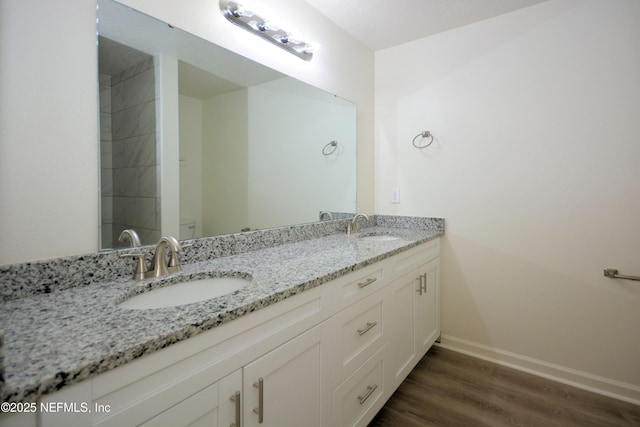 bathroom featuring a sink, baseboards, wood finished floors, and double vanity