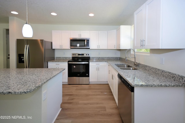 kitchen with light stone countertops, a sink, stainless steel appliances, white cabinets, and light wood-type flooring