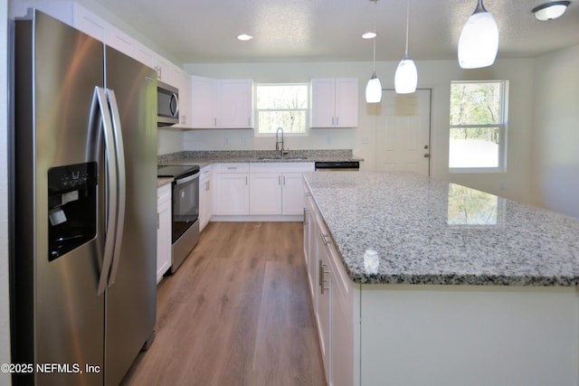 kitchen with a sink, a center island, appliances with stainless steel finishes, white cabinets, and light wood finished floors