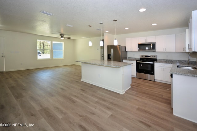 kitchen with light wood-style flooring, a sink, open floor plan, appliances with stainless steel finishes, and ceiling fan