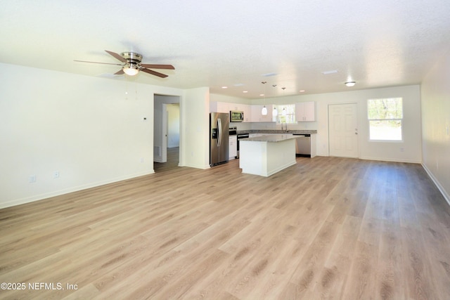 kitchen featuring a center island, open floor plan, stainless steel appliances, white cabinetry, and a ceiling fan