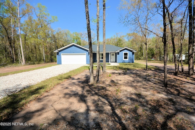 ranch-style house with gravel driveway, an attached garage, and a view of trees