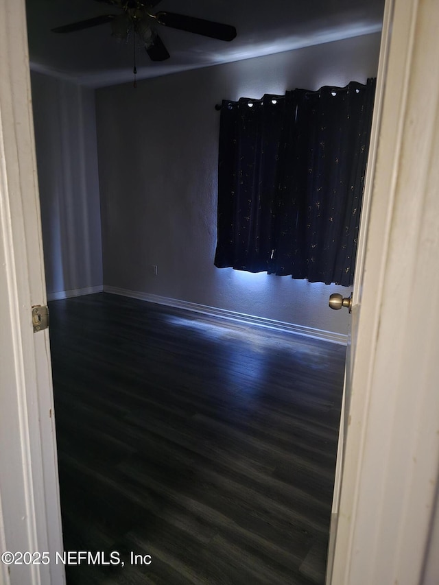 empty room featuring wood finished floors, a ceiling fan, and baseboards