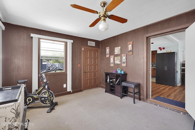 exercise area with visible vents, ceiling fan, carpet flooring, and wood walls