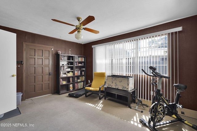 sitting room with wood walls, carpet, and ceiling fan