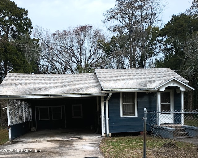 ranch-style house with a carport, concrete driveway, fence, and roof with shingles