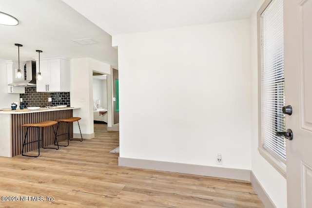 kitchen featuring visible vents, light wood-type flooring, a breakfast bar, wall chimney range hood, and tasteful backsplash