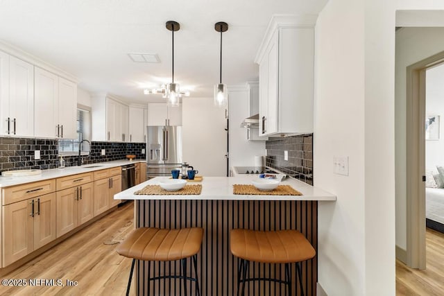 kitchen featuring stainless steel refrigerator with ice dispenser, a sink, under cabinet range hood, a peninsula, and light wood finished floors