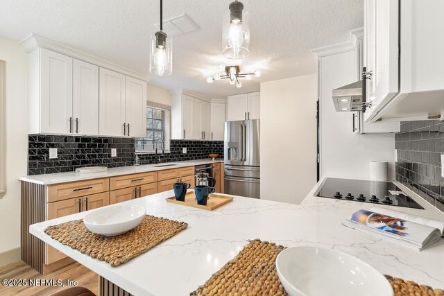 kitchen with high end fridge, a sink, a peninsula, black electric stovetop, and light stone countertops