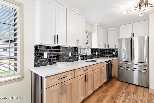 kitchen featuring backsplash, light stone countertops, light wood-style flooring, stainless steel fridge, and a sink