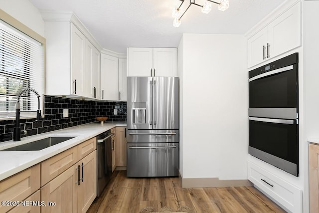 kitchen with backsplash, light stone counters, light wood-style flooring, appliances with stainless steel finishes, and a sink