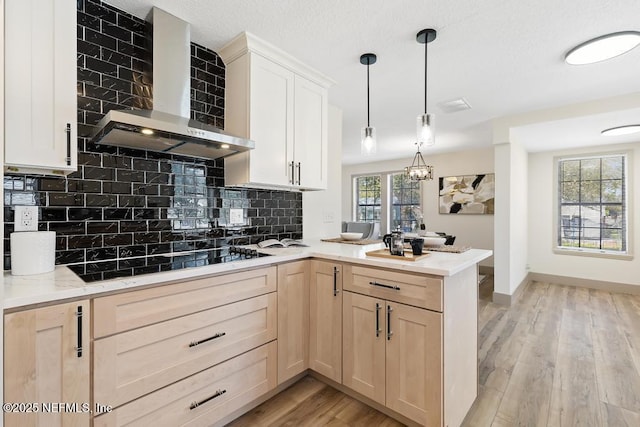 kitchen featuring light wood finished floors, wall chimney range hood, light brown cabinetry, a peninsula, and black electric cooktop