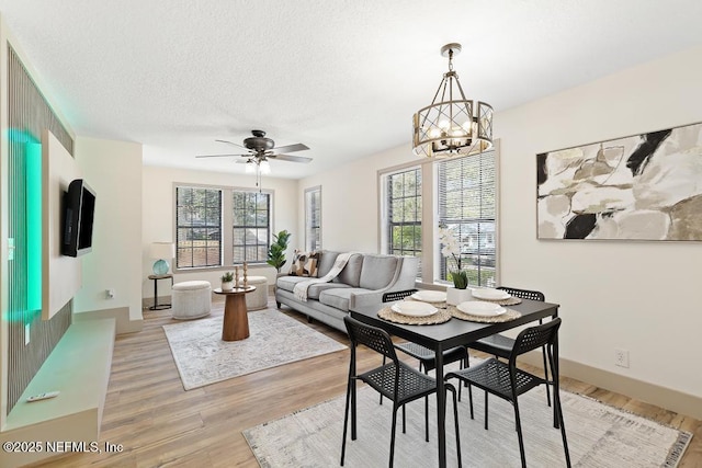 dining area with ceiling fan with notable chandelier, light wood-style flooring, a textured ceiling, and baseboards