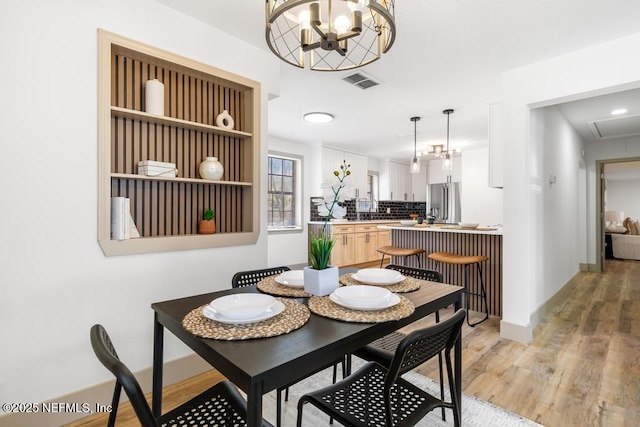 dining room featuring baseboards, light wood-style floors, visible vents, and a chandelier