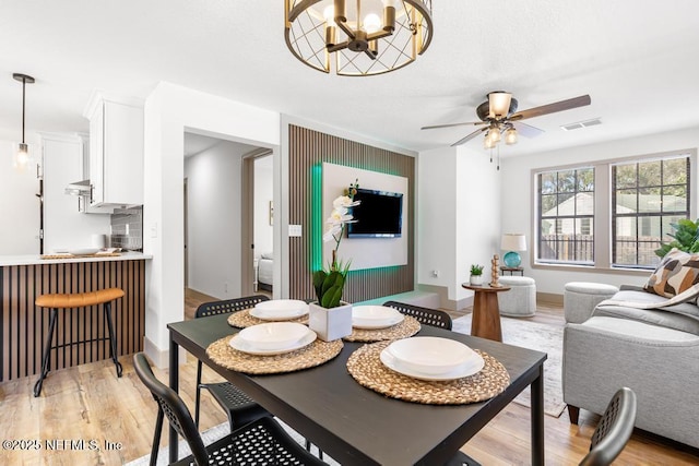 dining space featuring light wood finished floors, visible vents, and ceiling fan with notable chandelier