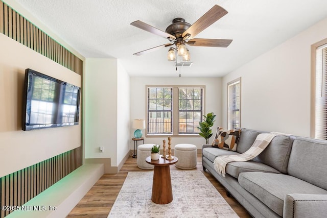 living area featuring visible vents, a textured ceiling, wood finished floors, and a ceiling fan