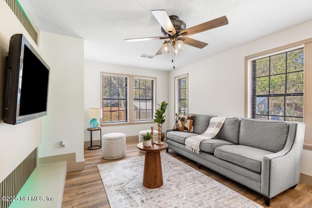 living area with visible vents, a ceiling fan, a textured ceiling, wood finished floors, and baseboards