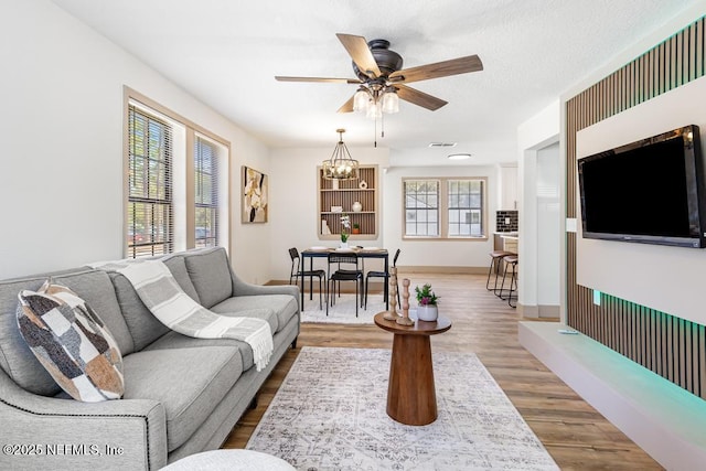 living room featuring wood finished floors, baseboards, visible vents, a textured ceiling, and ceiling fan with notable chandelier