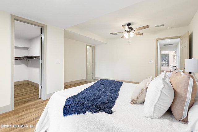 bedroom with baseboards, visible vents, ceiling fan, a walk in closet, and light wood-type flooring