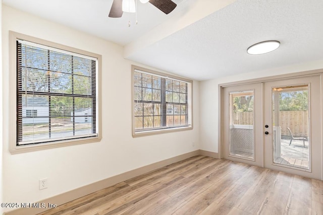 unfurnished room featuring a ceiling fan, baseboards, light wood finished floors, french doors, and a textured ceiling