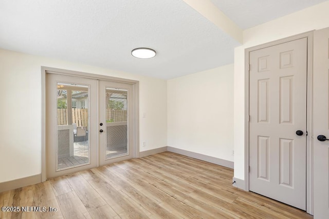 empty room with french doors, baseboards, a textured ceiling, and light wood-style flooring