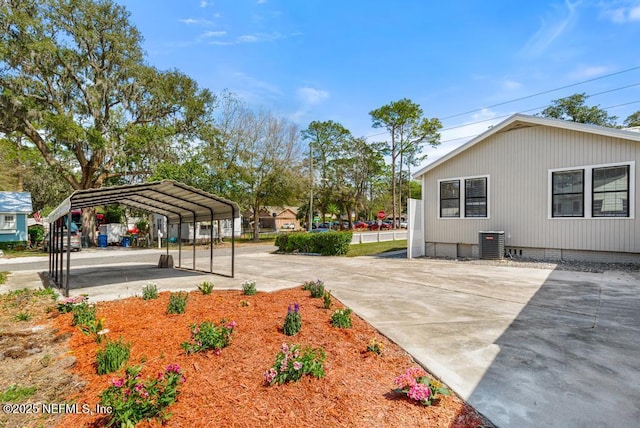 view of yard with a carport, central AC unit, and concrete driveway