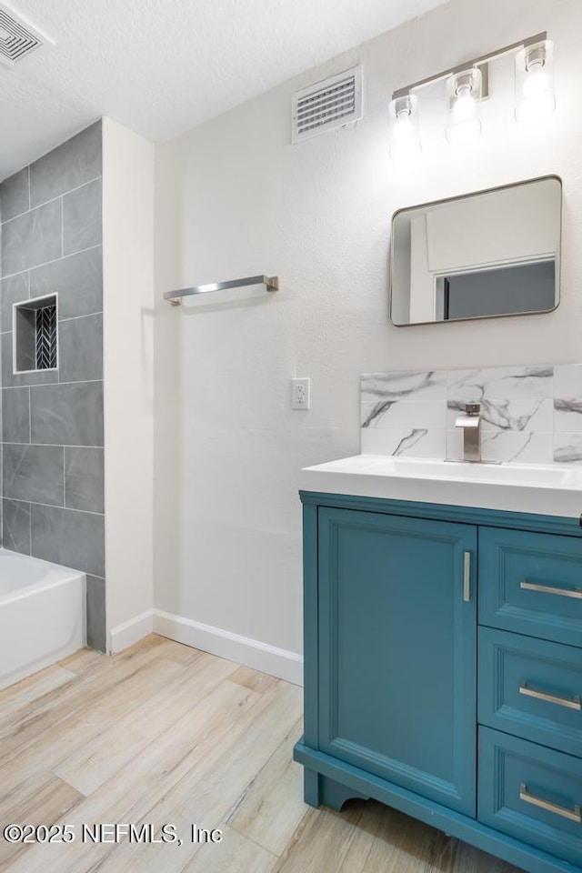 bathroom featuring visible vents, baseboards, vanity, wood finished floors, and a textured ceiling