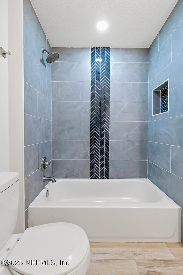 full bathroom with a textured ceiling, toilet, and washtub / shower combination