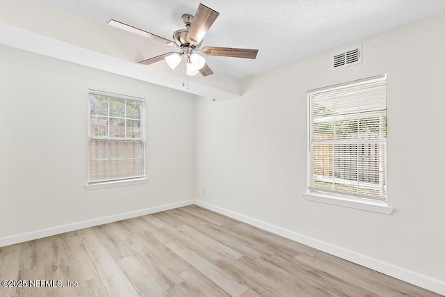 spare room featuring light wood finished floors, visible vents, a ceiling fan, and baseboards