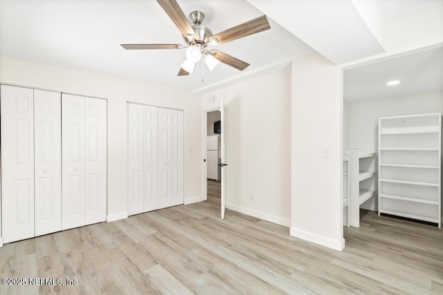 unfurnished bedroom featuring baseboards, two closets, wood finished floors, and freestanding refrigerator