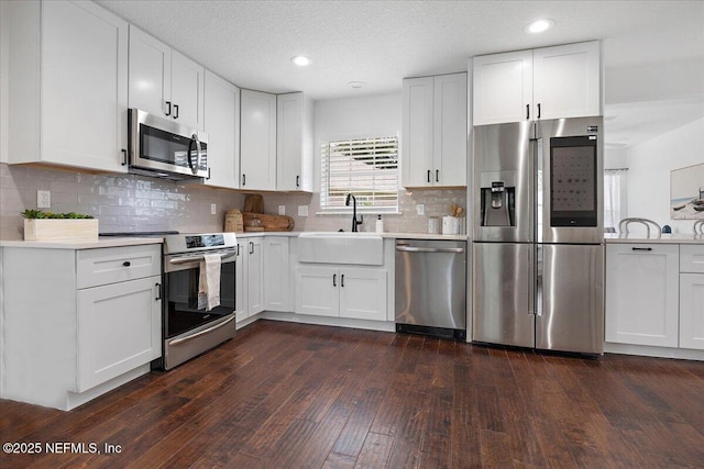 kitchen featuring dark wood-type flooring, light countertops, stainless steel appliances, white cabinetry, and a sink