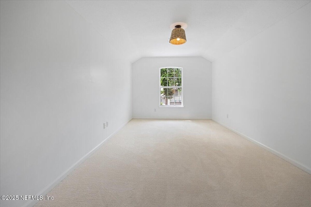 spare room featuring vaulted ceiling, carpet, and baseboards