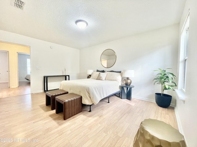 bedroom featuring visible vents, baseboards, a textured ceiling, and light wood finished floors