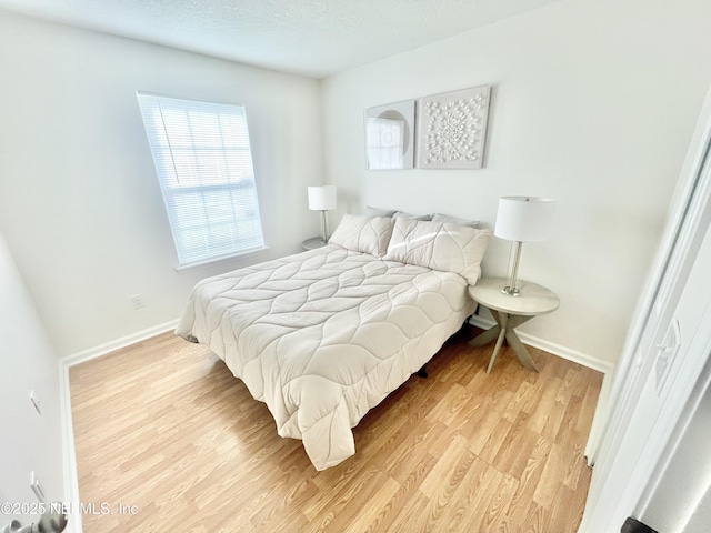 bedroom featuring a textured ceiling, baseboards, and light wood-style floors