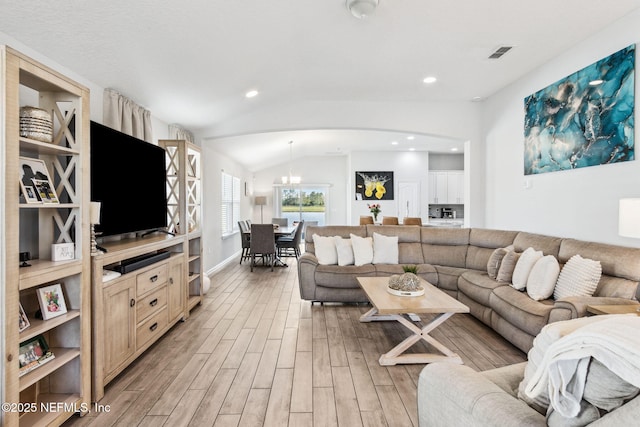 living area with visible vents, a chandelier, vaulted ceiling, light wood-style floors, and arched walkways