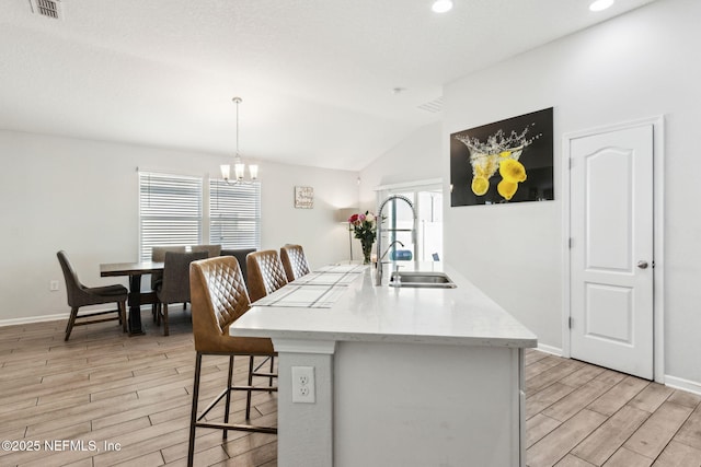 kitchen with visible vents, wood finish floors, a chandelier, vaulted ceiling, and a sink