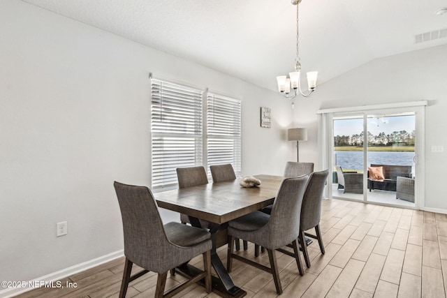 dining area with wood finish floors, visible vents, a water view, an inviting chandelier, and vaulted ceiling