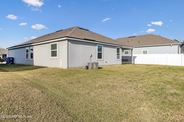 back of property with central AC unit, a yard, fence, and a shingled roof