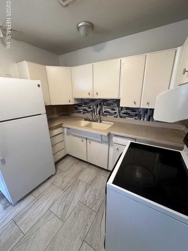 kitchen featuring range with electric cooktop, decorative backsplash, freestanding refrigerator, white cabinetry, and a sink