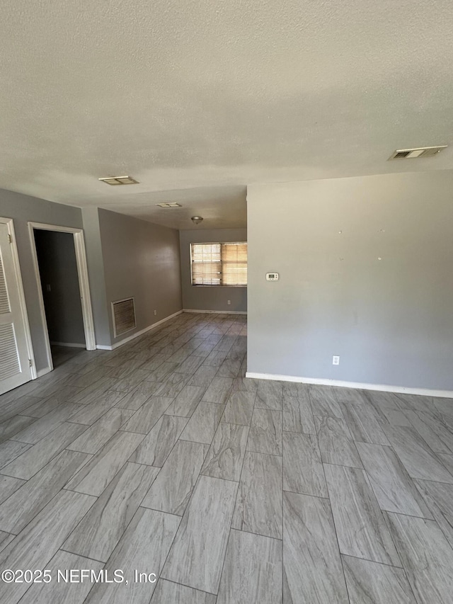 empty room with baseboards, visible vents, and a textured ceiling