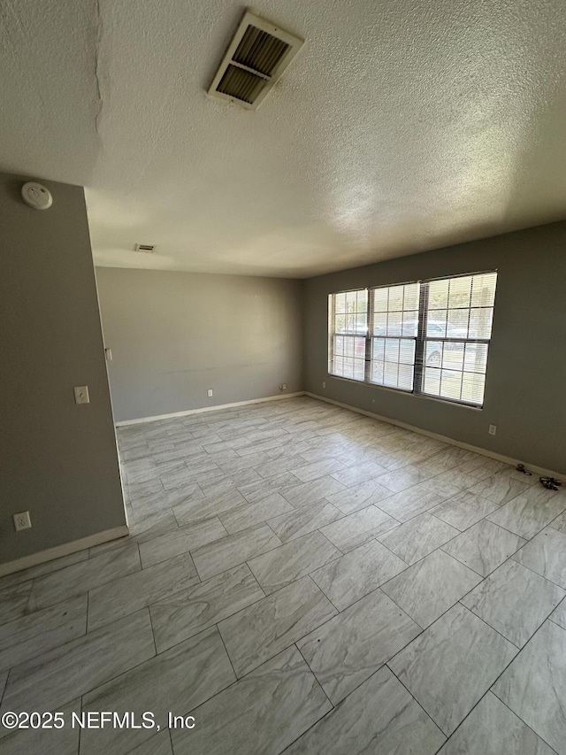 unfurnished room featuring baseboards, visible vents, and a textured ceiling